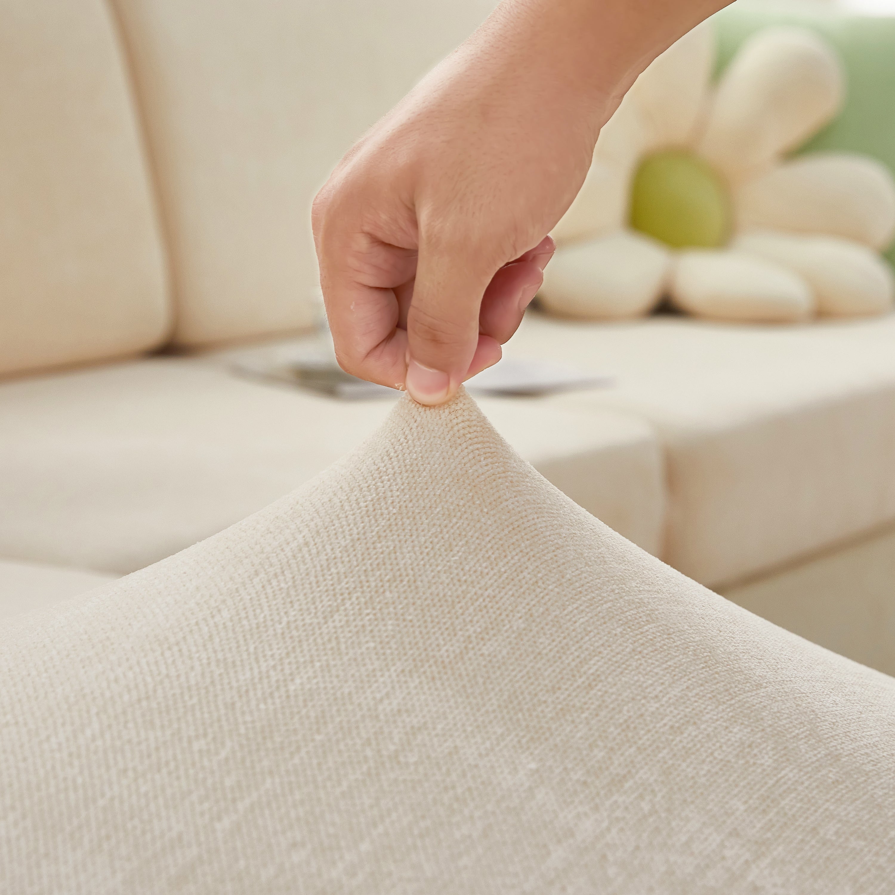 Stretchy FancySofas Chenille bankhoes in de kleur Ivory Beige, toont elasticiteit en pasvorm door de stof omhoog te trekken.